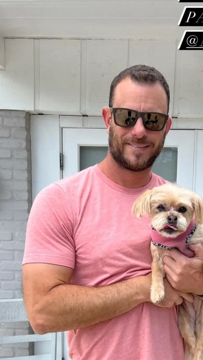 A man holding a small dog outside a home